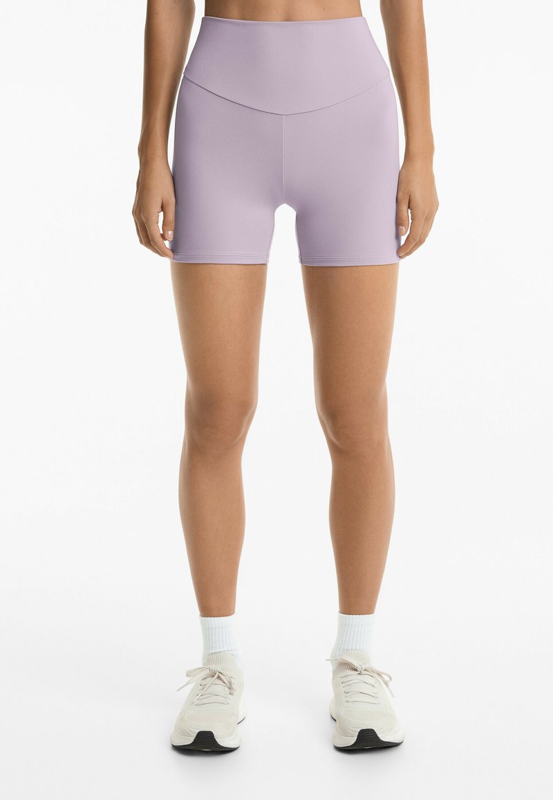 Lilac shortsit, joissa on korkea vyötärö ja jotka on valmistettu sileästä, venyvästä materiaalista. Niissä on tiukka malli ja ne ulottuvat reiden keskikohtaan.