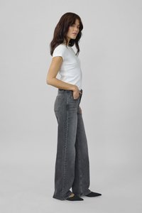 Jeans de pierna ancha en denim gris oscuro con una cintura alta, que cuentan con bolsillos delanteros y traseros, combinados con una camiseta ajustada blanca y bailarinas negras.