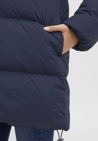 Námořnická puffer bunda se sametovou prošívanou texturou, boční kapsou a elastickými manžetami. Nastavitelný stahovací šnur na spodním okraji.