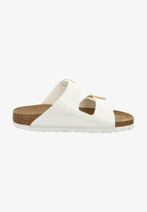 White slide sandals with two wide straps, cork footbed, textured outsole, and subtle gold hardware accents. Flat design with open toe.