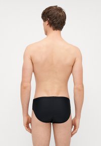Bañadores negros con cintura elástica, textura suave y un diseño ajustado que muestra un estilo minimalista. Vista trasera exhibida.