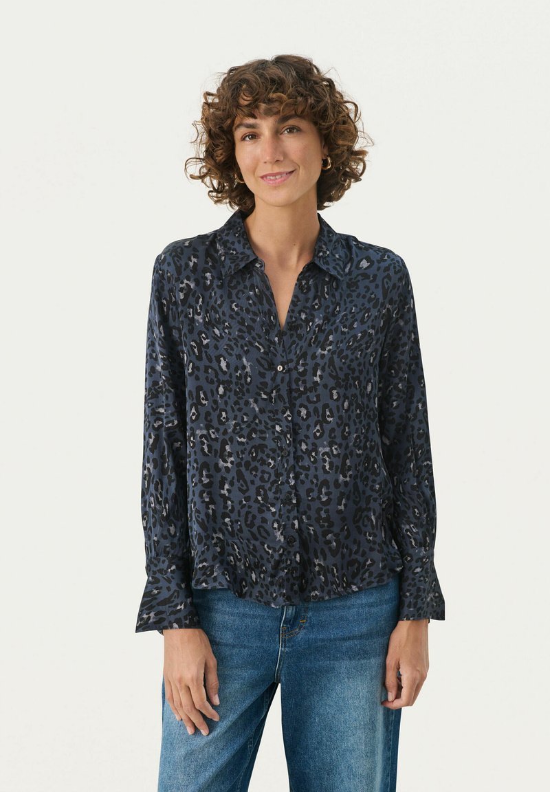 Mørkeblå skjorte med knapper og leopardmønster, lange ærmer og krave, lavet af et glat stof. Båret med lyseblå jeans.