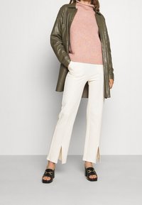 Olivgrön läderjacka, rosa stickad polotröja, vita split-bukser och svarta slidesandaler med detaljer i guld.