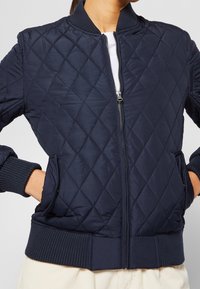 Navy quilted bomber jacket with diamond pattern, ribbed cuffs and hem, front zipper, and side pockets, made of smooth, lightweight fabric.