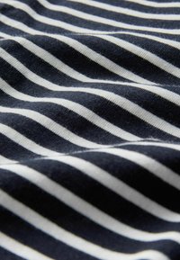 Detailný záber na čierne a biele horizontálne pruhované tkaniny s jemnými riasami a textúrovaným pleteným vzorom.