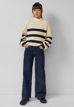 Knitted cream sweater with black horizontal stripes, paired with high-waisted dark blue wide-leg jeans and black platform boots.
