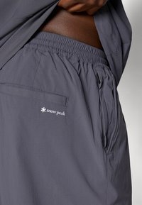 Gray elastic-waist shorts featuring a side pocket, rear pocket, and a white "snow peak" logo. Smooth fabric with a lightweight texture.