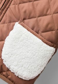 Gequilte bruine stof met een witte fleece zak. De zak heeft een textuurrijke, donzige oppervlakte die contrasteert met de gladde buitenlaag.