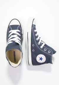Para granatowych wysokich trampek Converse z białymi sznurowadłami i gumowymi podeszwami, jeden but stoi wyprostowany, a drugi leży na boku.