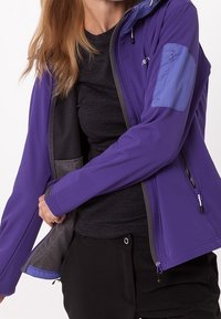 Lila Softshelljacke mit tailliertem Design, kontrastierendem blauen Akzent am Ärmel und funktionalen Reißverschlusstaschen. Texturiertes, leichtes Material.
