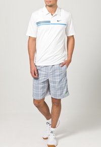 White polo shirt with a blue horizontal stripe, paired with gray plaid shorts. The outfit features a Nike logo and a pocket detail.