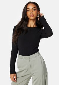 Top nero a maniche lunghe a coste abbinato a pantaloni verdi chiari. Dettagli notevoli includono maniche aderenti e scollo rotondo.