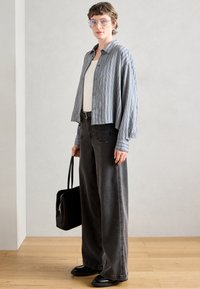 Lys blå og hvidstribet skjorte med knapper, hvid tanktop, mørkegrå højtaljede brede bukser, sort tote taske, sorte sko.