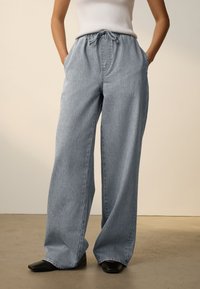 Pantalon en denim bleu clair à jambes larges avec une taille élastique et un cordon de serrage. Comprend des poches latérales et une coupe décontractée.