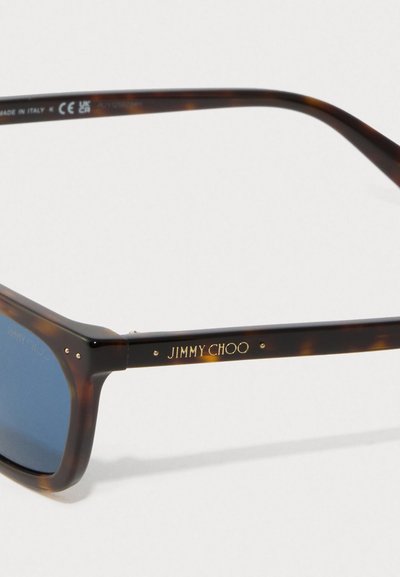Tortoiseshell sunglasses arm with gold "JIMMY CHOO" logo and blue tinted lens detail, made in Italy, with CE and UKCA markings.