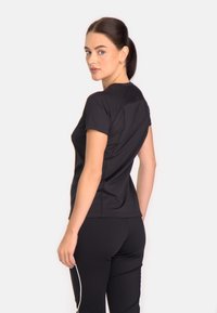 Melnas īsām piedurknēm sporta krekls ar gludu tekstūru, slim fit piegriezumu un smalku šuvju detaļām, saskaņots ar atbilstošām melnām biksēm.