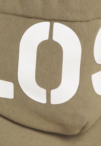 Gros plan d'un tissu beige avec un grand chiffre zéro blanc imprimé partiellement visible.
