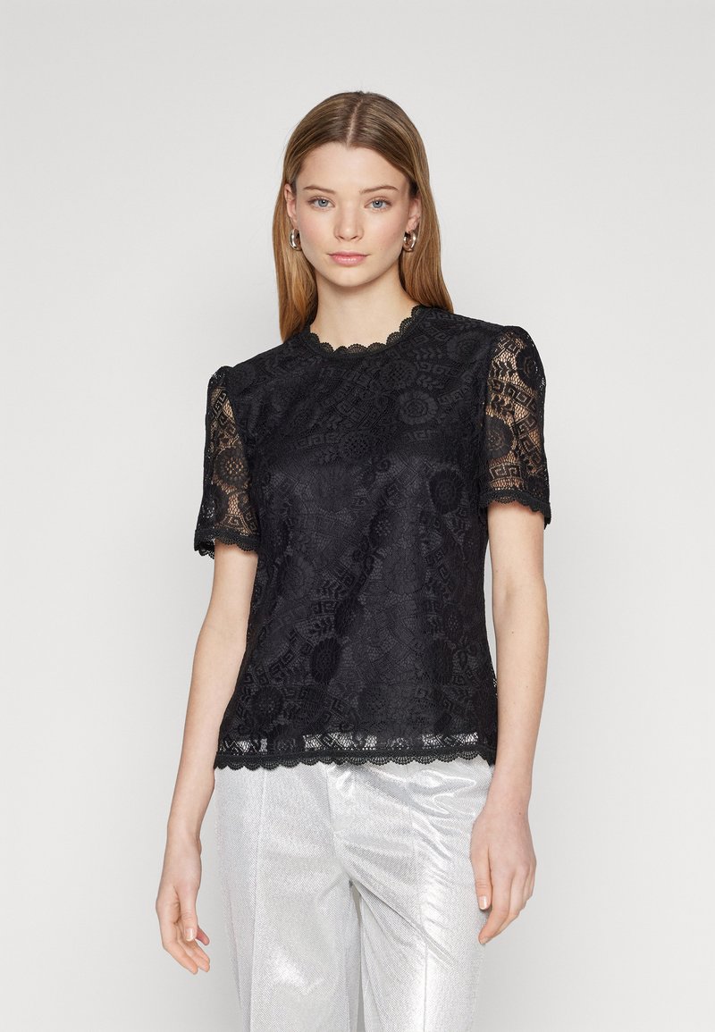 Zwarte kanten top met korte mouwen, gegolfde halslijn, textuur met bloempatroon en kanten rand aan de zoom, gestyled met zilveren broeken.