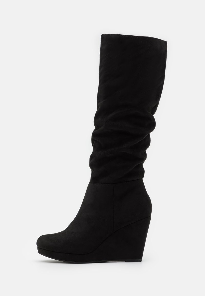 Bottes noires en suede montantes à talon compensé avec un haut décontracté, bout rond et texture lisse. Le talon compensé ajoute de la hauteur et de la stabilité.
