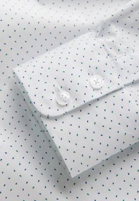 Camisa de algodón blanca con un pequeño patrón repetido de formas de lágrima en azul y verde. Presenta puños con botones y botones blancos.