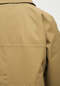 Εγγύς πλάνο πίσω μέρους ταμπά μπουφάν με ανάγλυφο λογότυπο The North Face στην περιοχή της ωμοπλάτης.