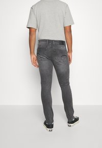 Jeans de mezclilla gris con un corte ajustado, bolsillos traseros y una etiqueta negra en la cintura, combinados con zapatillas casuales negras.