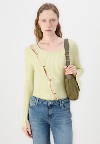 Ljusgrön ribbad jumper med långa ärmar, med djup rundad halsringning och utskärningsdesign prydd med guldiga accenter. Matchad med blå jeans.