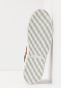 Bruna lädersneakers med en vit gummisula. Sulan har horisontella spår för grepp och har en präglad logotyp på sig.