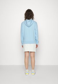 Ljusblå hoodie med dragsnodd i huvan, ribbade ärmslut och nederkant, i kombination med en vit kjol och sneakers med gula och blå accenter.