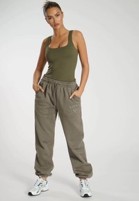 Olivgrön linne och grå joggers med en "Aspen Colorado"-logotyp. Joggers har elastisk midja och sidfickor. Vita sneakers.