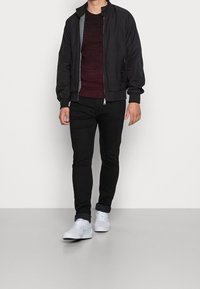 Svart bomberjacka med rutigt foder, vinröd tröja, svarta jeans och vita sneakers. Utformad för avslappnad stil med en sportig look.