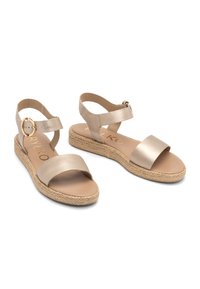 Metallic kuld avatud varvastega sandaalid kahekordse rihmaga; üks rihm on kaunistatud dekoratiivse klambriga. Espadrilli stiilis kudumine platvormi talla.