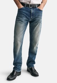 Blå denimjeans med en blekt tvätt, rak passform, femficksdesign, parat med svarta läderskor och ett svart bälte.