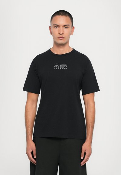 T-shirt nera, maniche corte, scollatura rotonda, con stampa grafica bianca che presenta numeri e un design circolare al centro del petto.