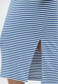 Μπλε και λευκή φούστα με οριζόντιες ρίγες, με σκάσιμο μπροστά στο ύψος του γονάτου που δείχνει τμήμα του ποδιού.