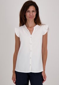 Witte blouse met korte mouwen, rimpelachtige schouders, knoopsluiting aan de voorkant, zachte katoenen stof en een relaxte pasvorm, gecombineerd met donkere broek.