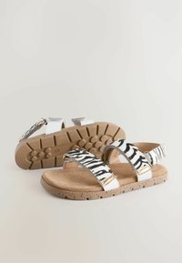Sandali con stampa zebra in bianco e nero con accenti metallici, sottopiedi imbottito beige e suola in gomma testurizzata. Due cinturini regolabili.