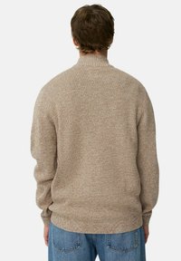 Beige textuurtrui met een hoge kraag en lange mouwen, voorzien van een rib patroon. Draagt lichtblauwe jeans.