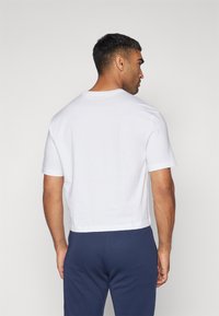 T-shirt bianca in cotone con scollatura rotonda e maniche corte, caratterizzata da un design cropped. Indossata con pantaloni blu navy.
