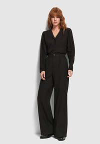 Camicia nera con bottoni e scollatura a V, rifinita con pizzo, abbinata a pantaloni neri a gamba larga a vita alta, dotati di un bottone e tasche.