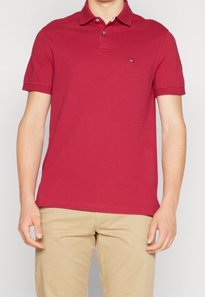 Polo rouge en coton, doté d'un col classique, de manches courtes et d'un petit logo sur la poitrine. Texture lisse et coupe ajustée.