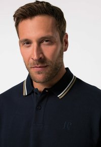 Marineblaues Poloshirt aus strukturiertem Stoff, mit einem Kragen mit zwei Streifen in Beige und Creme sowie einem kleinen gestickten Logo auf der Brust.