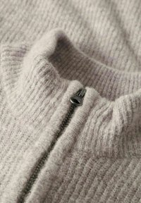 Jasnoszary sweter zapinany na zamek z ribbowym wzorem, wysoki kołnierz i czarny metalowy zamek błyskawiczny. Miękki, ciepły materiał.