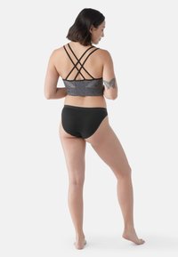 Bralette sportivo nero con retro grigio a fantasia e molteplici cinghie incrociate; abbinato a slip da bikini neri. Tessuto liscio e elastico.