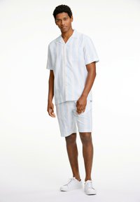 Conjunto de pijama ligero de mangas cortas en blanco con rayas azules; incluye un bolsillo en la camiseta y pantalones cortos a juego. El tejido parece transpirable.