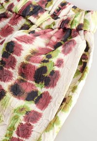 Orezaný textil s vráskovou textúrou, s kvetinovým vzorom v marhuľovej, zelenej a čiernej farbe na krémovom pozadí. Elastický pás.
