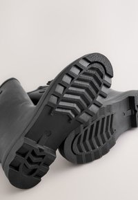 Sorte gummistøvler med en tekstureret ydersål med sildebenmønster, glat overdel med rundet snude og forstærket hæl.