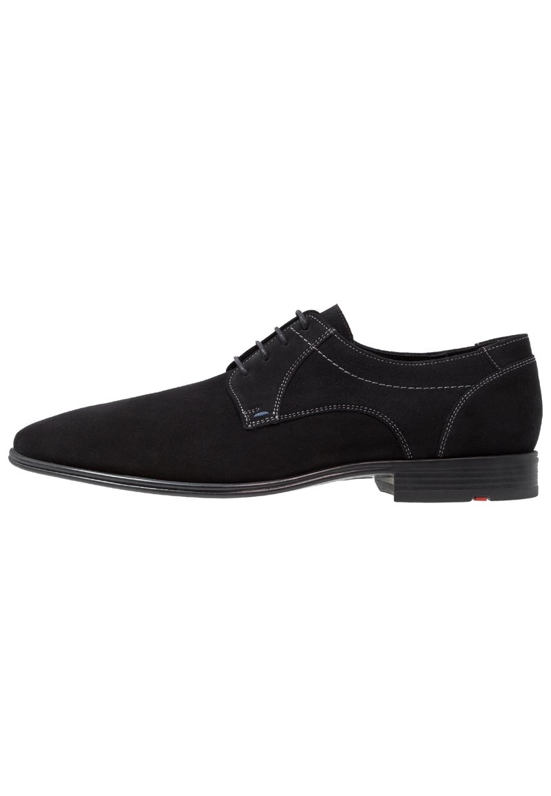 Chaussure noire en suède à lacets avec un profil bas, présentant des coutures contrastantes et une semelle lisse. Design simple avec un bout arrondi.