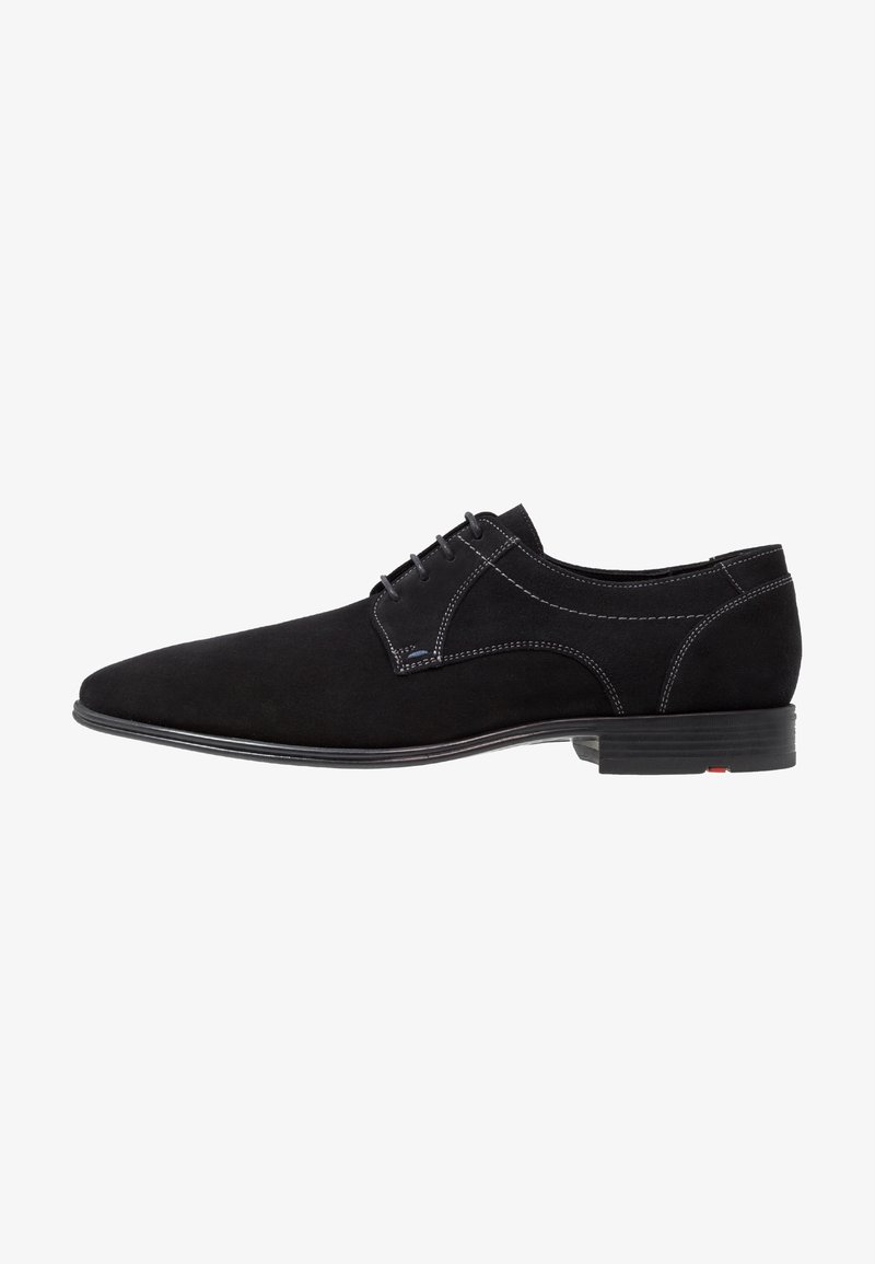 Chaussure noire en suède à lacets avec un profil bas, présentant des coutures contrastantes et une semelle lisse. Design simple avec un bout arrondi.