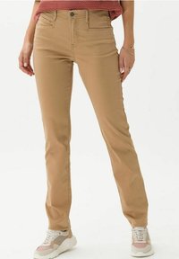 Pantalons en mélange de coton beige avec une coupe droite, poches avant et un système de fermeture à bouton en métal, associés à des baskets grises et roses.